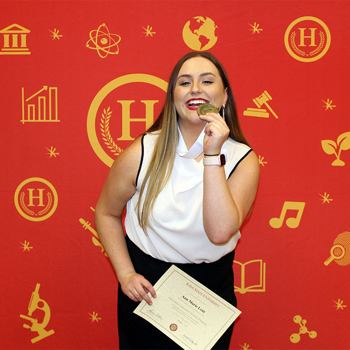 Ann Marie Lent holding up her honors certificate and playfully biting her honors medal.